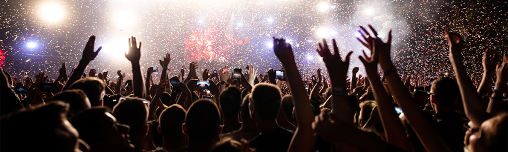 A packed concert has the crowd all raising their arms in the air to celebrate the end of a performance. Confetti it pouring down from the sky across the crowd.